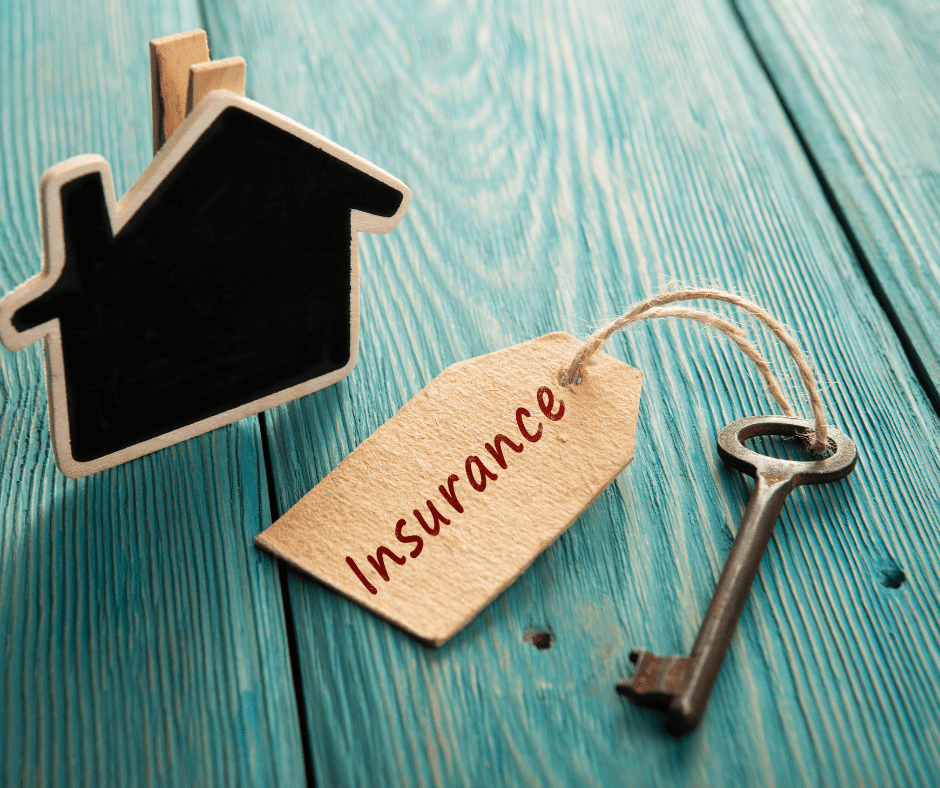 a cute out of a house and a key on a wooden table with an insurance tag