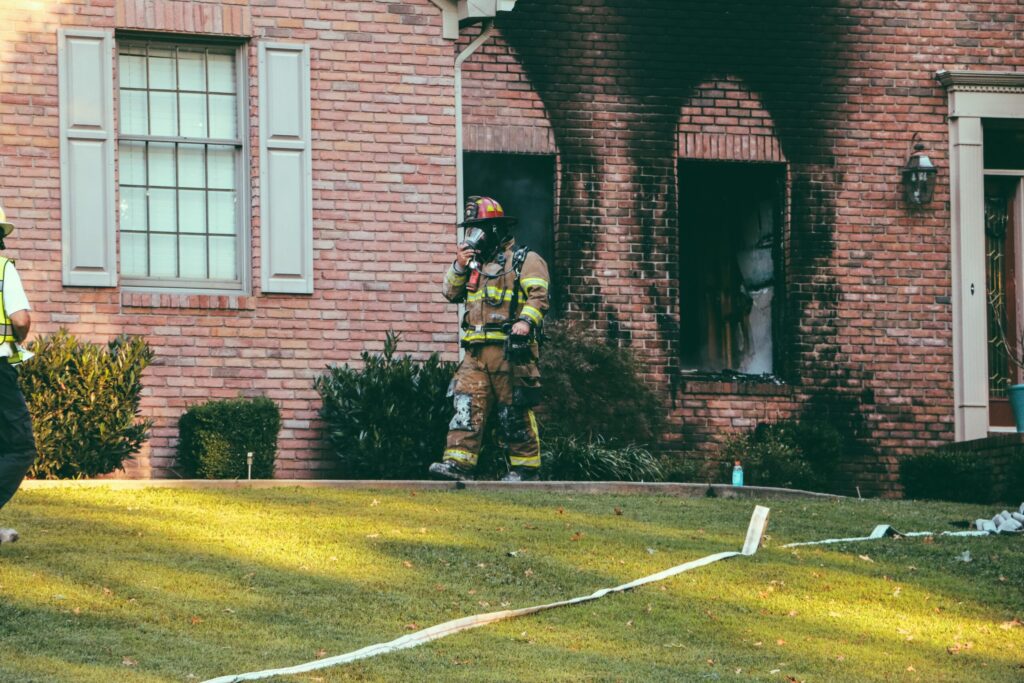 fire fighter walking in front of smoke damage coming out of windows of a brick home in denver
