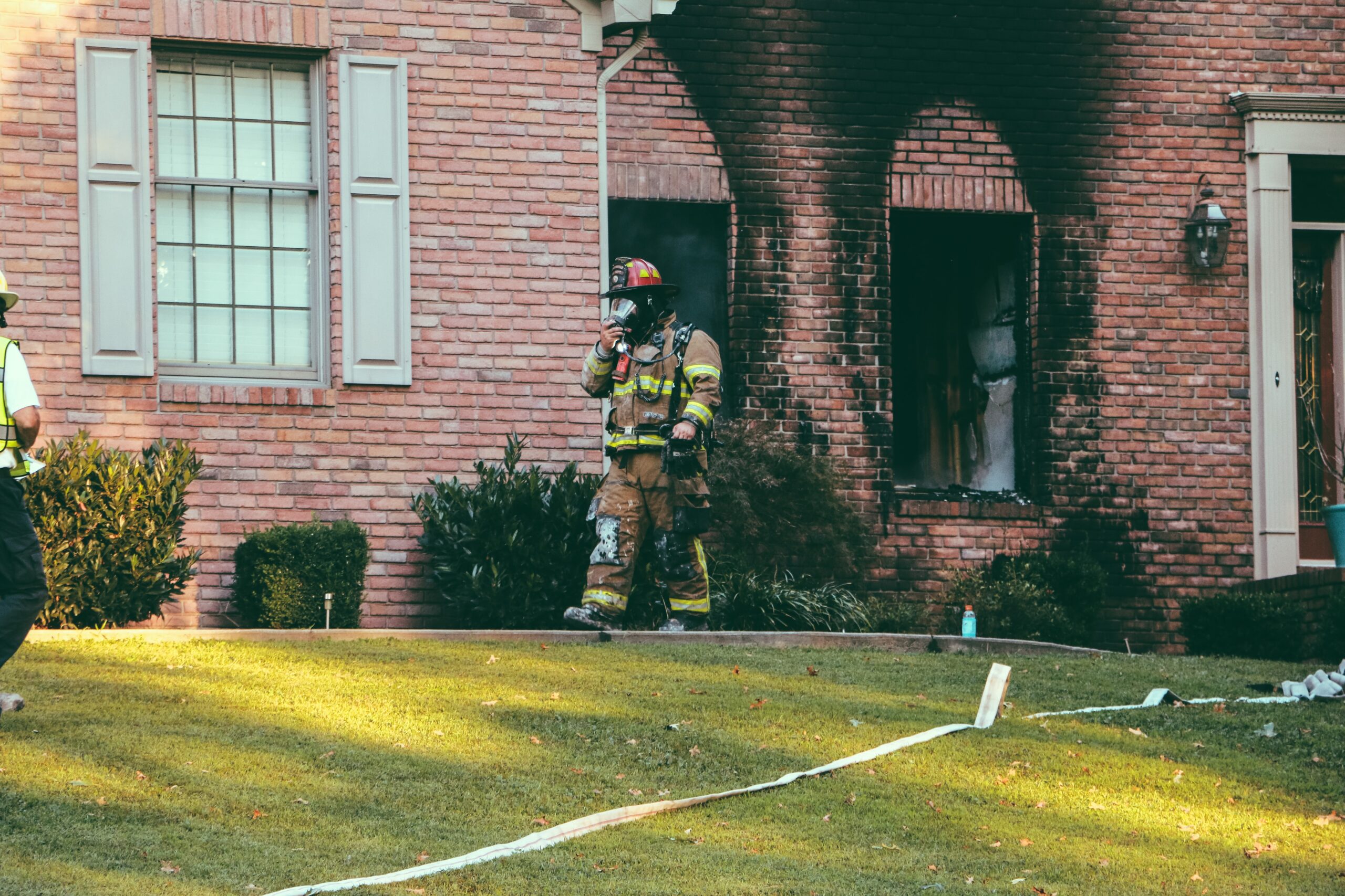 fire fighter walking in front of smoke damage coming out of windows of a brick home in denver