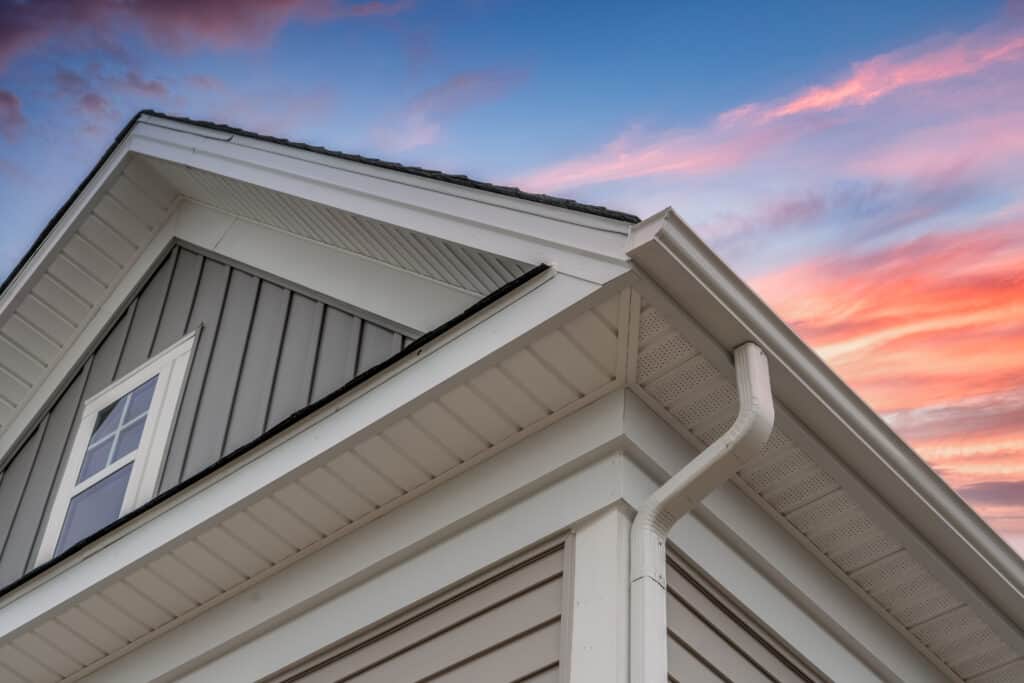 corner of house with sunset sky in the background, shot shows a drip edge with gutter and downspout after roofing installation by charlotte roofing contractor