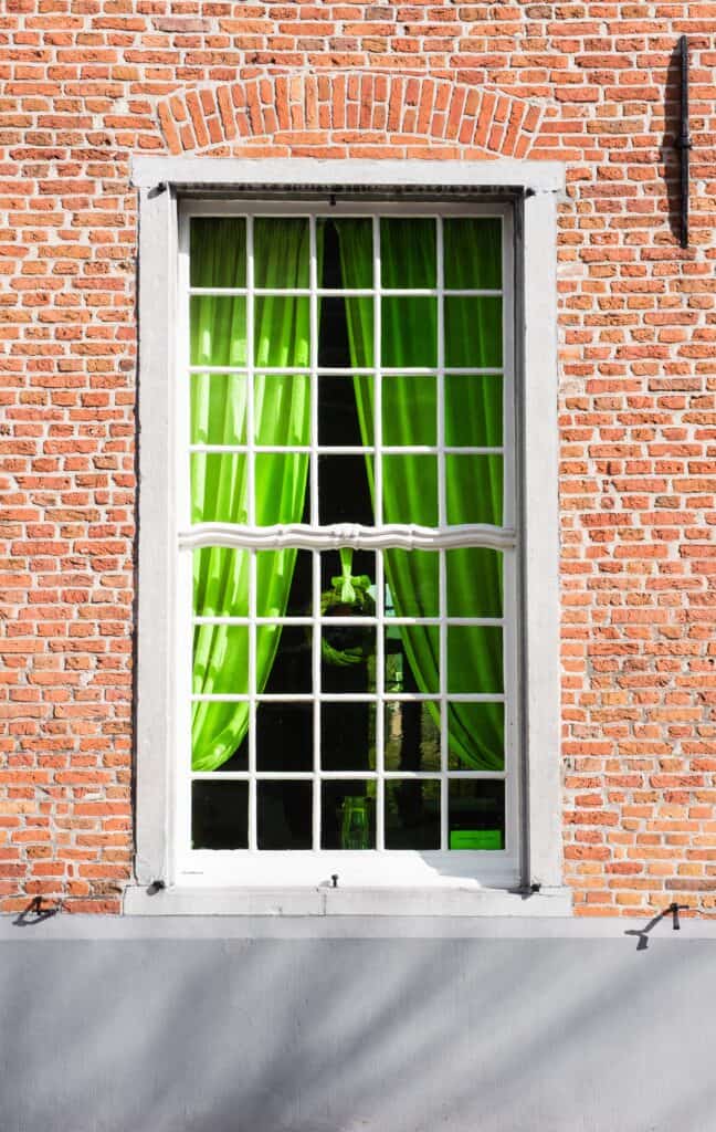 A brick building with bright green drapes behind the window.
